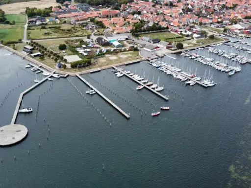 Luftaufnahme des Marstal Hafens mit vielen Segelbooten, die an Stegen liegen. Ein ovaler Steg mit Bänken ragt ins Wasser.