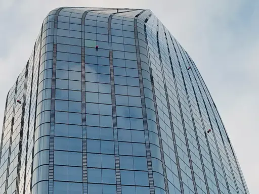 Trabajadores en altura limpian ventanas de edificio moderno. Sikaflex para que sirve: sellar y unir, asegurando la integridad de estas estructuras.