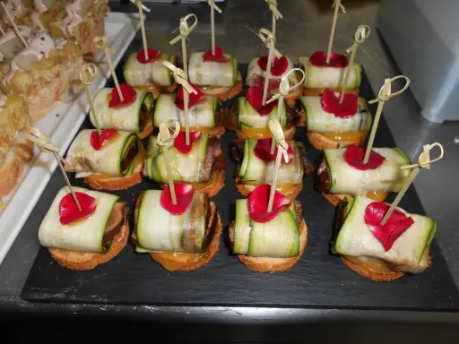Variedad de tipos de pinchos con calabacín enrollado, pétalos rojos y palillos de bambú.