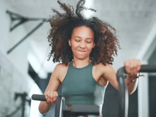 Frau mit lockigem Haar trainiert intensiv auf einem Fahrrad. Sie gibt alles, was ist HIIT – High Intensity Interval Training.