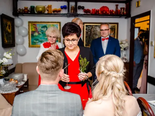 Rodzina udziela błogosławieństwa młodej parze. Kobieta trzyma gałązkę ziół, symbolizującą pomyślność.