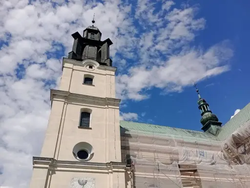 Wieża kościoła w Gidlach pod błękitnym niebem z chmurami. Widać fragment dachu w rusztowaniach.