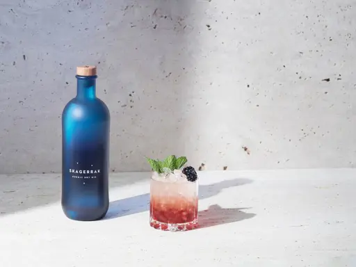 En blå flaska Skagerrak Nordic Dry Gin bredvid en läcker bramble drink med björnbär och mynta.