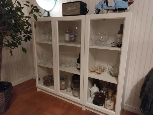 Ett DIY-projekt med ett vitt Billy vitrinskåp fyllt med glas, flaskor och dekorationer.
