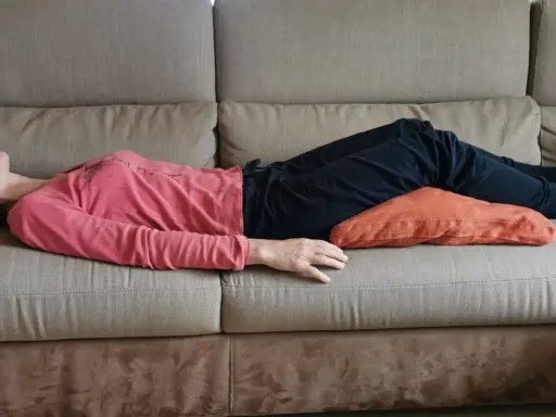 Donna sdraiata sul divano con un cuscino sotto le ginocchia per una postura corretta seduti divano.
