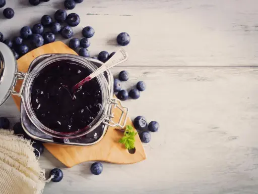 Frische Heidelbeeren und selbstgemachte Heidelbeermarmelade im Glas, bereit zum Genießen.