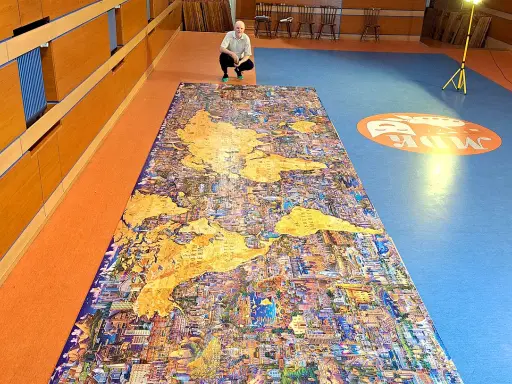 Mężczyzna kuca przy największych puzzlach na świecie, przedstawiających mapę świata z detalami miast.