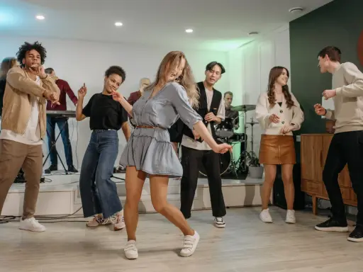 Luźne stylizacje na domówkę: jeansy, sukienka, spódniczka i sweter. Wszyscy tańczą i bawią się przy muzyce.