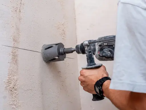 Persona taladra hormigón con una broca de corona. La marca en la pared indica dónde perforar.