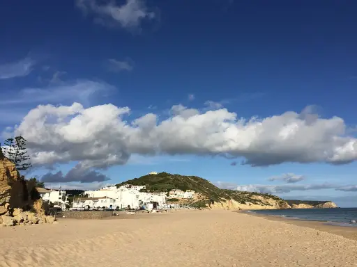 Sonne, Sand und weiße Häuser: Ein malerischer Blick auf Salema, Portugal, mit dem Atlantik und dramatischen Wolken.