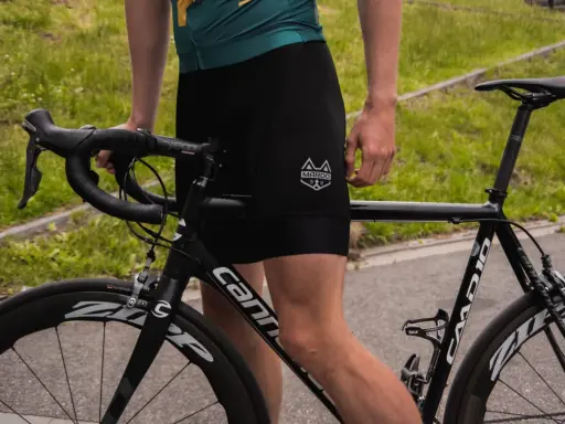Kolarz w czarnych spodenkach i zielonej koszulce przygotowuje się do treningu kolarskiego. Rower szosowy Cannondale czeka na jazdę.