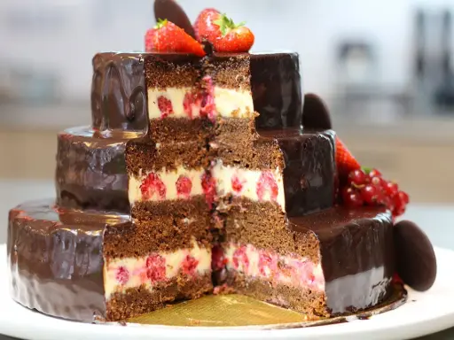 Gâteau à trois étages au chocolat et aux framboises, parfait pour une recette gâteau anniversaire facile. Décoré de fruits rouges et de chocolat.