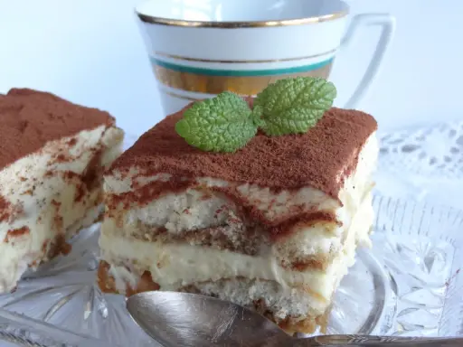 Pyszne tiramisu bezglutenowe, posypane kakao i udekorowane listkiem mięty, czeka na łyżeczkę.