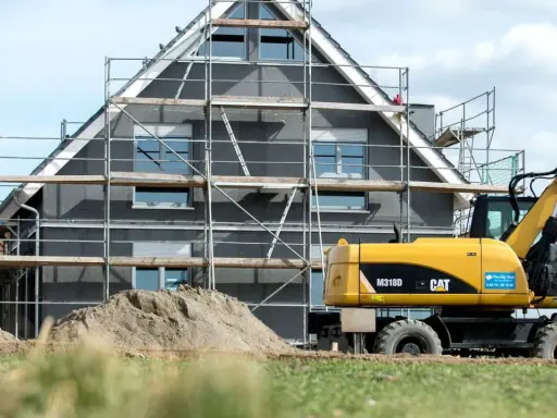 Ein Haus im Bau mit Gerüst und einem Bagger. Die bauseitigen Leistungen sind im vollen Gange.