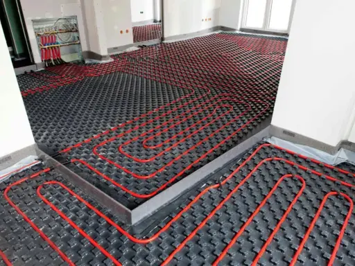 Instalación de suelo radiante con tuberías rojas sobre paneles negros, preparado para aerotermia.