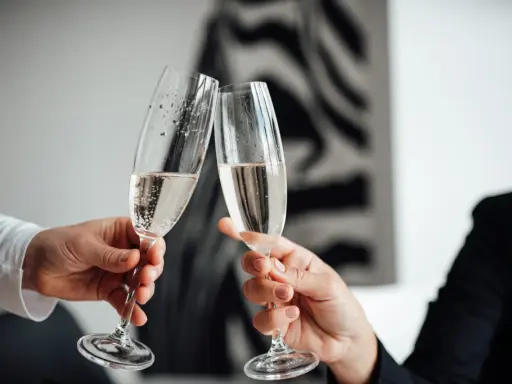Dwie dłonie unoszą kieliszki z szampanem do toastu. To idealny moment na świętowanie srebrnych godów.