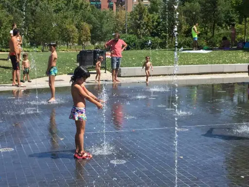 Niños y adultos disfrutan del agua en las fuentes del madrid rio parque.