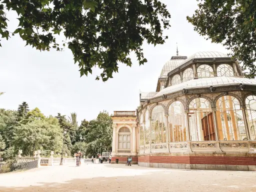 Ein sonniger Tag im Retiro Park. Menschen spazieren vor dem Palacio de Cristal, einem beeindruckenden Glaspalast.