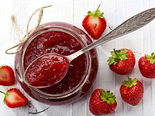 Glas mit Erdbeermarmelade, gesüßt mit Xylit, daneben frische Erdbeeren und ein Löffel Marmelade.