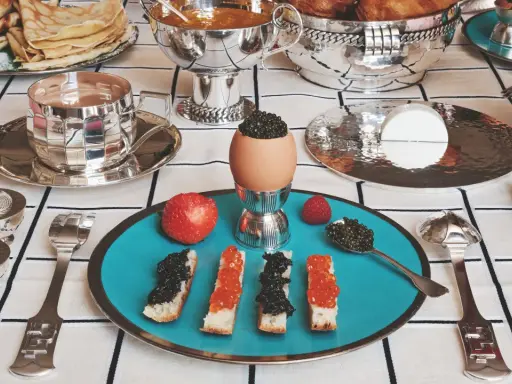 Un service de table à la française élégant pour un petit-déjeuner luxueux : toasts au caviar, œufs, fruits et crêpes.