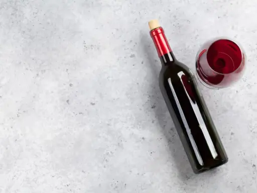 En flaska tamaral vin och ett glas rött vin på ett grått, stenig bakgrund.