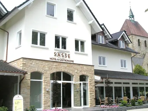 Gasthof Sasse in Soest mit Hotel & Gastronomie-Schild, Steinfassade und Kirche im Hintergrund.