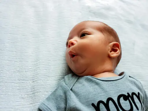Noworodek z lekkim kręczem szyi i asymetrią twarzy, w szarym body z napisem "mom".