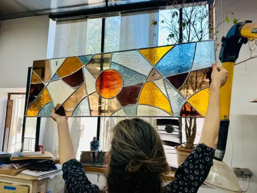 Un artiste admire son œuvre, un vitrail aux couleurs chaudes et géométriques, fruit d'un cours de vitrail.