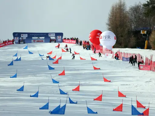 Zawodnicy snowboardu pokonują trasę z czerwonymi i niebieskimi tyczkami na stoku Jaworzyny Krynickiej.