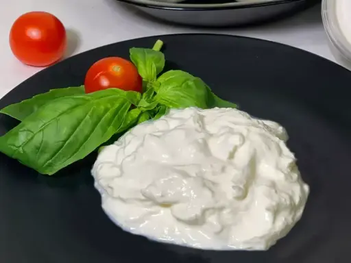 En krämig hög av stracciatella ost med färska basilikablad och körsbärstomater på en svart tallrik.