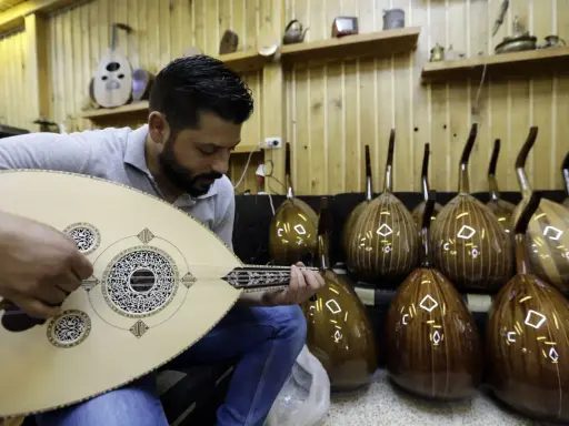 Un joueur de oud expérimenté accorde son instrument, entouré d'autres ouds prêts à être joués.
