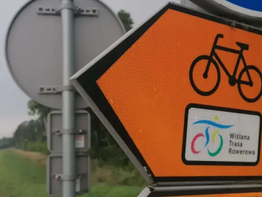 Pomarańczowy znak kierunkowy z rowerem i napisem "Wiślana Trasa Rowerowa" zapowiada podróż ścieżką wzdłuż rzeki.