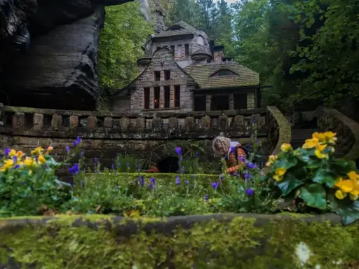 Kamienny domek w sercu czeskiej Szwajcarii, otoczony zielenią i kwitnącymi kwiatami.