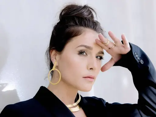 Jessie Ware, w czarnej marynarce, z dłonią na czole, jakby prosiła "say you love me". Złote kolczyki i naszyjnik dodają blasku.