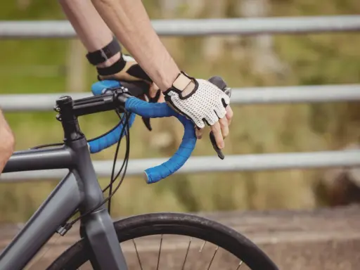 Rowerzysta w rękawiczkach trzyma kierownicę. Czas przekroczyć prog mleczanowy i przyspieszyć.