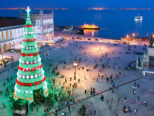 Lisbona illuminata per il weekend dell'Immacolata: un imponente albero di Natale brilla in una piazza affollata, con il fiume e le luci della città sullo sfondo.