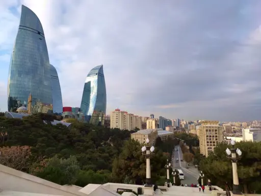 Płomienne wieże Flame Towers w Baku, które warto zobaczyć, górują nad miastem. W tle widać panoramę miasta i zielone drzewa.