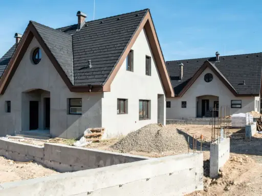 Nowe domy z betonu w budowie, z ciemnymi dachami i jasnymi ścianami, na tle błękitnego nieba.