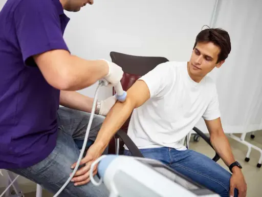 Fizjoterapeuta stosuje terapię falą uderzeniową na ramieniu pacjenta, aby złagodzić ból i przyspieszyć regenerację.