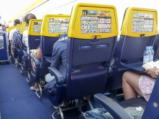 Wnętrze samolotu Boeing 737, rzędy miejsc dla pasażerów. Widok na siedzenia z żółtymi oparciami i instrukcjami bezpieczeństwa.