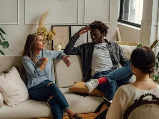 Pareja discutiendo en terapia, buscando soluciones a su **crisis de pareja**. La mujer gesticula, el hombre escucha con la mano en la cabeza.