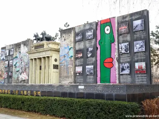 Fragment muru berlińskiego z graffiti i zdjęciami, obok replika Bramy Brandenburskiej.