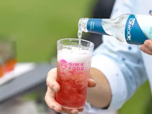 Tonic water wird in ein Glas mit rotem Getränk gegossen. Perfekt, um den Sommerdrink zu mischen.