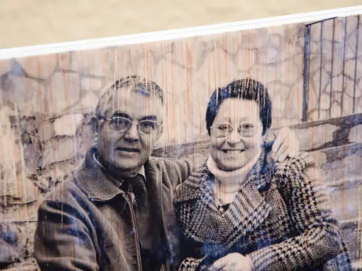 Pareja sonriente en un retrato transferir foto a madera, con un fondo de ladrillos y textura de madera visible.