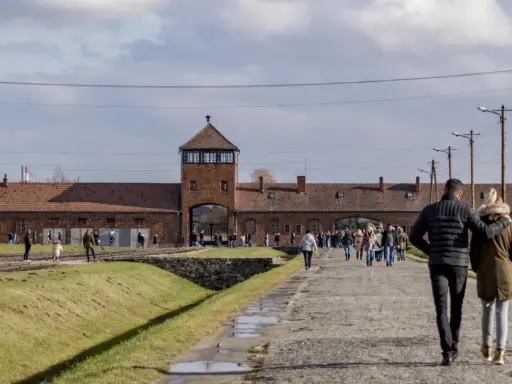 Spacer po terenie byłego obozu Auschwitz. Para idzie w stronę bramy z wieżą.