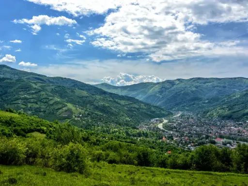 Zielone wzgórza Karpat na Ukrainie, z miasteczkiem w dolinie i rzeką.