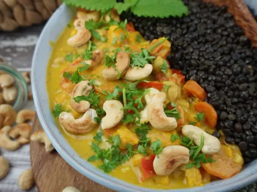Ein cremiges Beluga Linsen Curry mit Cashewkernen und frischer Petersilie, daneben eine Portion schwarzer Beluga Linsen.