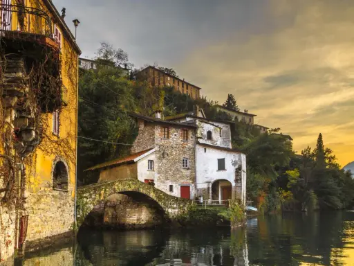 Malerische Häuser am Wasser in Nesso am Comer See, mit einer alten Steinbrücke und goldenem Abendlicht.
