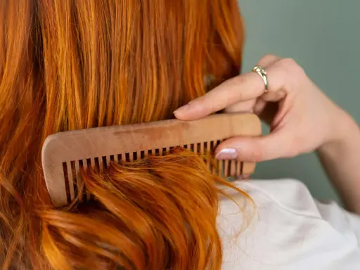 Mujer peina su cabello pelirrojo con un peine de madera. ¿En qué época del año se cae más el pelo? El otoño es conocido por ser el momento en que el cabello se cae más.