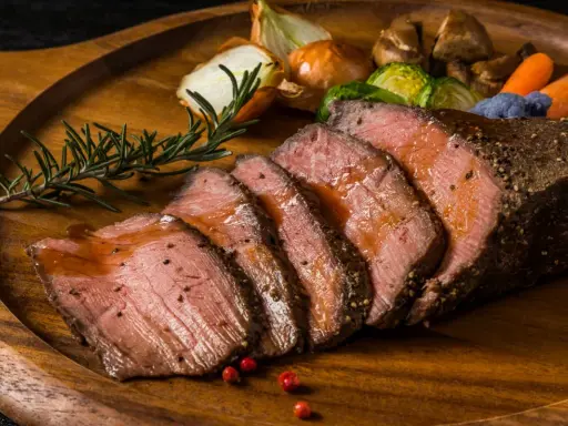 Succulento arrosto di manzo affettato, servito su un tagliere di legno con verdure arrosto, cipolle e rosmarino.